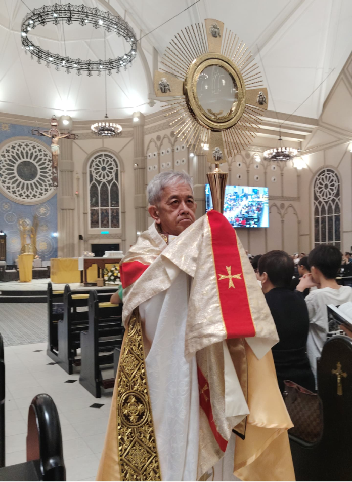 Rektor Gereja St Peter, Fr Vincent Chin, membawa Sakramen Maha Kudus dalam monstran sambil berarak mengelilingi gereja.